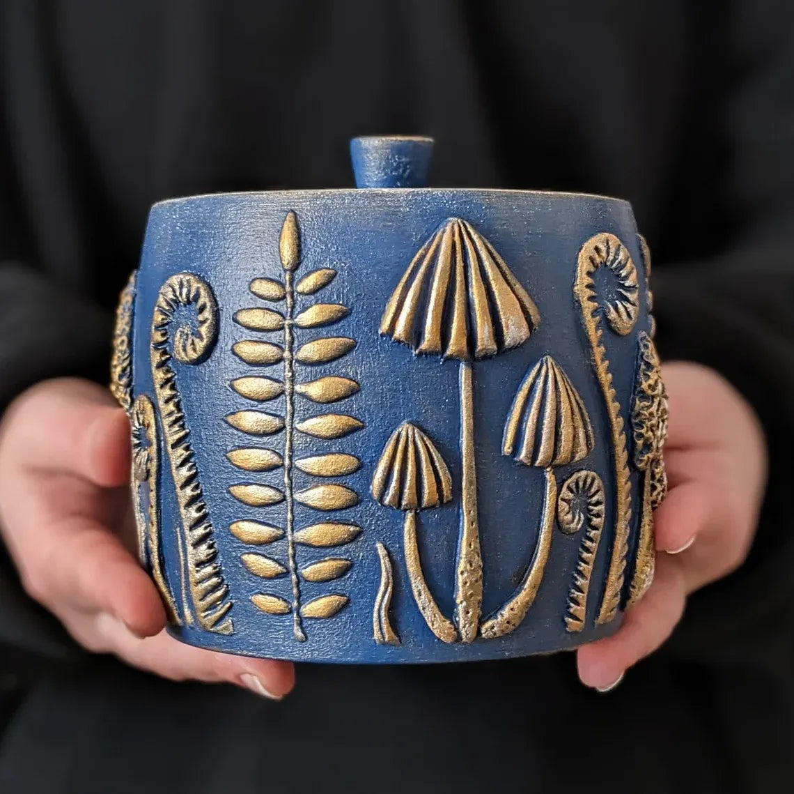 forest herbs and mushrooms blue wooden pot with lid in hands on dark background